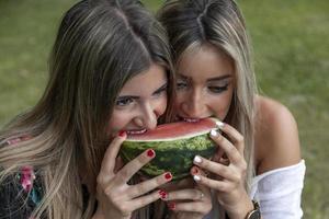 Paar von jung schön Frauen Essen ein Scheibe von frisch Wassermelone foto
