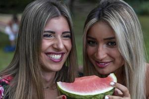 Paar von jung schön Frauen Essen ein Scheibe von frisch Wassermelone foto