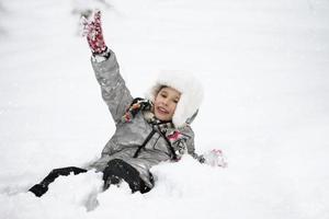 ein froh Junge im warm Kleider Lügen im das Schnee. Kind auf ein Winter gehen. foto