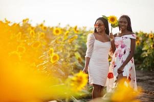 zwei hübsche junge schwarze Freunde Frau tragen Sommerkleid Pose in einem Sonnenblumenfeld. foto