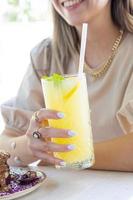 lächelnd Frau mit Weiß Nagel Polieren halten Limonade. kalt Limonade mit Zitrone und Minze. foto