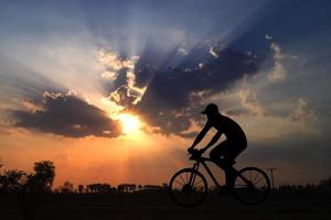 Schattenbild des Mannes, der ein Fahrrad im Sonnenuntergang reitet