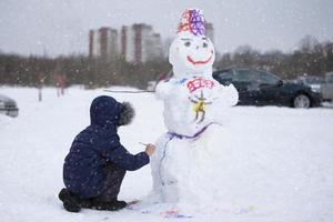 ein Junge Farben ein Schneemann auf ein Winter Tag. foto