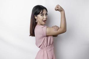 aufgeregt asiatisch Frau tragen ein Rosa Bluse zeigen stark Geste durch Heben ihr Waffen und Muskeln lächelnd stolz foto