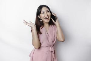 ein Porträt von ein glücklich asiatisch Frau gekleidet im Rosa und halten ihr Telefon, isoliert durch Weiß Hintergrund foto