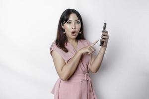 schockiert asiatisch Frau gekleidet im Rosa und halten ihr Telefon, isoliert durch Weiß Hintergrund foto
