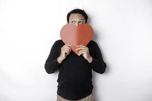 asiatisch Mann halten ein rot Papier Herz gestalten Abdeckung seine Gesicht. Valentinstag Konzept foto