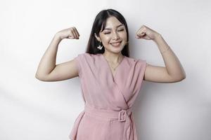 aufgeregt asiatisch Frau tragen ein Rosa Bluse zeigen stark Geste durch Heben ihr Waffen und Muskeln lächelnd stolz foto