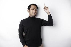 schockiert asiatisch Mann tragen schwarz Hemd zeigen beim das Kopieren Raum auf oben von ihn, isoliert durch Weiß Hintergrund foto