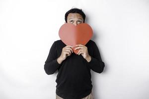 asiatisch Mann halten ein rot Papier Herz gestalten Abdeckung seine Gesicht. Valentinstag Konzept foto