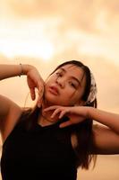 ein asiatisch Teenager tragen ein Weiß Bandana und schwarz Hemd mit ein sexy Ausdruck auf das Strand Sand foto