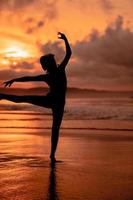 Silhouette von ein sehr schlank Ballerina tun Ballett trainieren allein auf das Strand mit Wellen abstürzen beim ihr foto