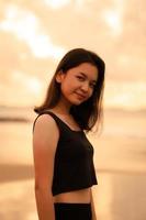 ein schön asiatisch Frau im schwarz Kleider ist genießen das Schönheit von das Strand mit ein lächelnd Ausdruck auf ihr Gesicht während auf Ferien foto