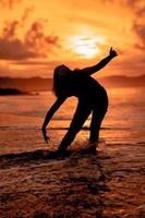 das Silhouette von ein indonesisch Teenager Tanzen sehr flexibel mit das abstürzen Wellen auf das Strand foto