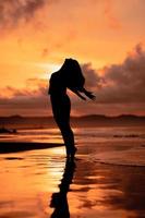 ein asiatisch Frau im Silhouette ist tun ein sehr schön tanzen auf das Strand mit das Wellen abstürzen foto