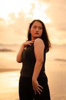 ein asiatisch Frau posieren mit ihr Hände angehoben und berühren ihr schwarz Haar leidenschaftlich auf das Strand foto