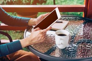 asiatisch Frau mit Tablette auf Tabelle und Kaffee im Garten mit Jahrgang getönt. foto