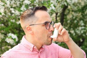 ein Mann Verwendet ein Inhalator zum Asthma, im das Park weil von ein Allergie - - ein Konzept zeigen das Auswirkungen von Verschmutzung, Krankheit und Krankheit foto