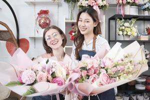 Porträt von zwei jungen, schönen Frauen, Floristenpartnern, die Blumenstrauß geben, lächeln und in die Kamera schauen, hübscher Unternehmer, glückliche Arbeit des Blumenladens, farbenfroher Blumenstraußladen. foto