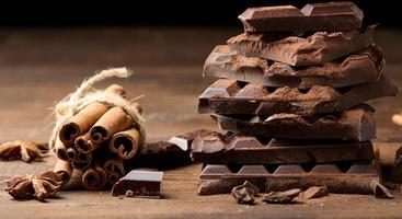 Bruchstücke von dunkler Schokolade, Zimtstangen und Sternanis auf einem braunen Holztisch foto