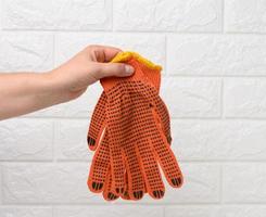 weiblich Hand hält Textil- Orange Arbeit Handschuhe auf ein Weiß Hintergrund foto