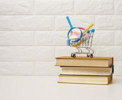 Miniatur Einkaufen Wagen steht auf ein Stapel von Bücher, Weiß Backstein Hintergrund, bestellen Bücher online foto