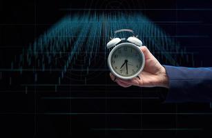Hand von ein Geschäftsmann hält ein runden Alarm Uhr auf das Hintergrund von Diagramme. das Konzept von Zeit ist Geld. foto