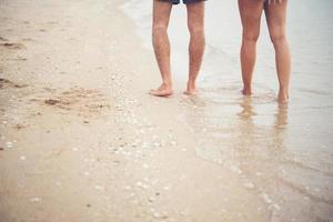 Rückseite des jungen Paares, das mit bloßen Füßen auf dem Strand geht foto