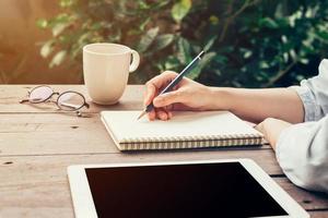 jung Geschäft Frau Hand mit Bleistift Schreiben auf Notizbuch. Frau Hand mit Bleistift Schreiben auf Notizbuch und Arbeiten beim Kaffee Geschäft. foto