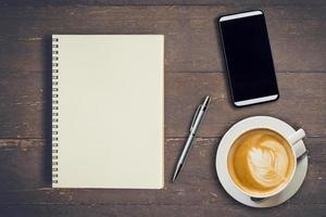 oben Aussicht Notizbuch, Stift, Kaffee Tasse, und Telefon auf Holz Tisch, Jahrgang Filter. foto