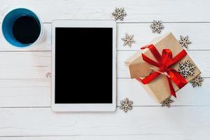 oben Aussicht Tablette, Tasse Kaffee, und Geschenk Box mit Schneeflocken auf Weiß Holz Hintergrund zum Weihnachten und Neu Jahr. foto