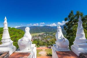 Weiß thailändisch Kunst Löwen beim Eingang von wat phra Das doi gongmu mit Aussicht von Maehongson Stadt im Abend Zeitraum foto