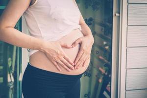 schwanger Frau halten Hand Herz gestalten zum Baby im ihr Bauch foto