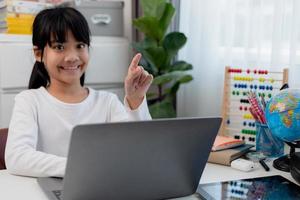 asiatische Schülerin macht ihre Hausaufgaben mit Laptop zu Hause. Kinder verwenden Gadgets zum Lernen. Bildung und Fernunterricht für Kinder. Homeschooling während der Quarantäne. Bleib zuhause foto