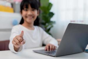 asiatische Schülerin macht ihre Hausaufgaben mit Laptop zu Hause. Kinder verwenden Gadgets zum Lernen. Bildung und Fernunterricht für Kinder. Homeschooling während der Quarantäne. Bleib zuhause foto