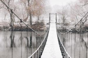 Fußgänger-Hängebrücke aus Stahl und Holz über den Fluss, Winter foto