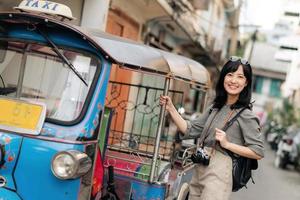 jung asiatisch Frau Rucksack Reisender Stehen ein Seite von Tuk Tuk Taxi auf Sommer- Urlaube beim Bangkok, Thailand. foto