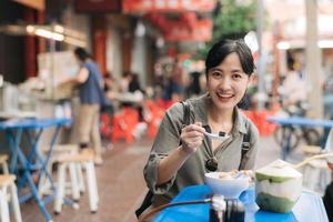 glücklich jung asiatisch Frau Rucksack Reisender genießen Straße Essen beim China Stadt, Dorf Straße Essen Markt im Bangkok, Thailand. Reisender Überprüfung aus Seite Straßen. foto