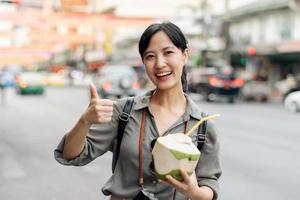 glücklich jung asiatisch Frau Rucksack Reisender Trinken ein Kokosnuss Saft beim China Stadt, Dorf Straße Essen Markt im Bangkok, Thailand. Reisender Überprüfung aus Seite Straßen. foto