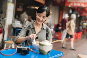 glücklich jung asiatisch Frau Rucksack Reisender genießen Straße Essen beim China Stadt, Dorf Straße Essen Markt im Bangkok, Thailand. Reisender Überprüfung aus Seite Straßen. foto