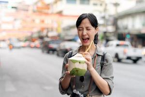 glücklich jung asiatisch Frau Rucksack Reisender Trinken ein Kokosnuss Saft beim China Stadt, Dorf Straße Essen Markt im Bangkok, Thailand. Reisender Überprüfung aus Seite Straßen. foto