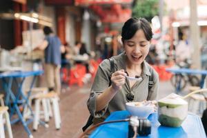 glücklich jung asiatisch Frau Rucksack Reisender genießen Straße Essen beim China Stadt, Dorf Straße Essen Markt im Bangkok, Thailand. Reisender Überprüfung aus Seite Straßen. foto