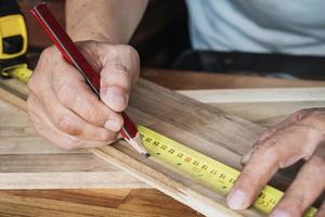 Zimmermann mit ein Messung Band und Kennzeichen ein Schnitt Linie mit Bleistift auf ein Holz board.diy Hersteller und Holzbearbeitung Konzept. selektiv Fokus foto