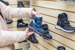 ein Frau im ein Jacke im ein Geschäft untersucht warm Kinder- Schuhe foto