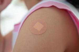 Geimpftes kleines asiatisches Mädchen mit Heftpflaster nach der Impfinjektion foto