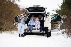 Familie mit Kinder sitzen auf Auto suv mit öffnen Kofferraum Stand im Winter Wald. foto