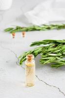 ein Flasche von Rosmarin wesentlich Öl und Kraut Geäst auf ein Teller auf das Tisch. organisch aromatisch natürlich Abhilfe. Vertikale Aussicht foto