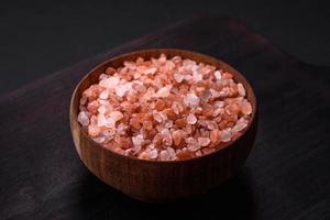Rosa Himalaya Salz- im ein hölzern Schüssel auf ein dunkel Beton Hintergrund foto