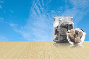 Münzen im ein Glas Krug auf Holz Fußboden ,Ersparnisse Münzen - - Investition und Interesse Konzept Speichern Geld Konzept, wachsend Geld auf Schweinchen Bank. isoliert auf Blau Himmel Hintergrund foto