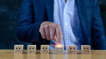 kundendienstbewertung und zufriedenheitsumfrage servicebewertungskonzepte.geschäftsmannhand wählen den holzblock mit dem glücklichen gesichtslächelngesichtssymbol auf holzwürfel. foto